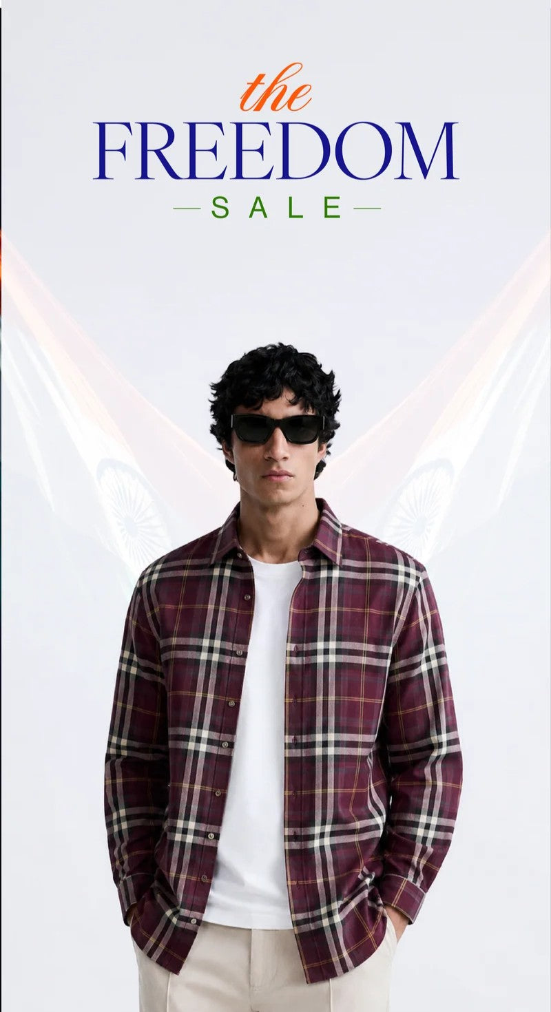 A man wearing a burgundy and black plaid button-down shirt over a white t-shirt and beige pants, standing against a white background with 'the FREEDOM SALE' text at the top.